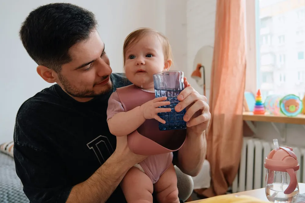 Otwarty kubeczek z czystą wodą obok butelki wody źródlanej z etykietą oznaczającą, że jest odpowiednia dla niemowląt — właściwy wybór napoju w okresie rozszerzania diety