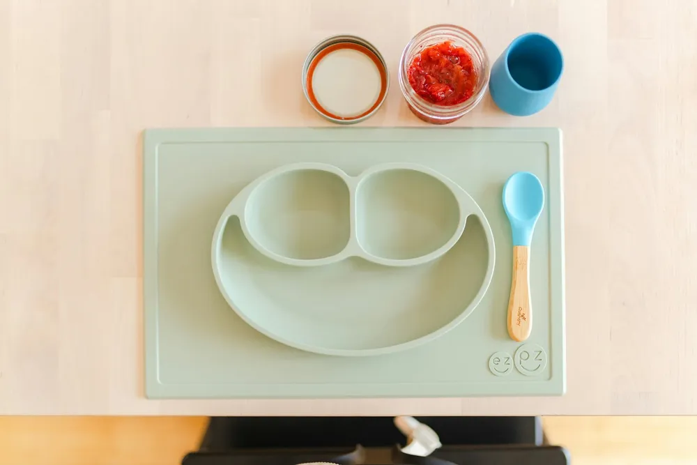 Trzy małe miseczki ustawione obok siebie na drewnianym blacie: jedna z gładkim puree warzywnym, druga z puree owocowym, trzecia z zupką warzywno-mięsną — ilustracja stopniowego wprowadzania kolejnych grup produktów