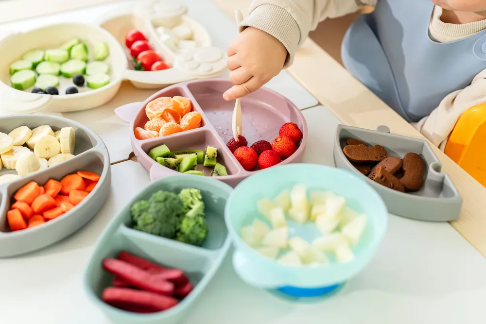 Niemowlę w krzesełku do karmienia jedzące łyżeczką gładkie warzywne puree z miseczki — radosne ujęcie zamykające temat pierwszych posiłków uzupełniających