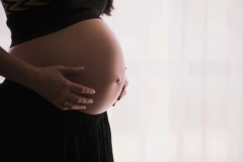Kobieta w ciąży przy stole z różnorodnym, kolorowym posiłkiem złożonym z warzyw, owoców i pełnoziarnistych produktów — dieta mamy jako pierwszy etap kształtowania preferencji smakowych dziecka
